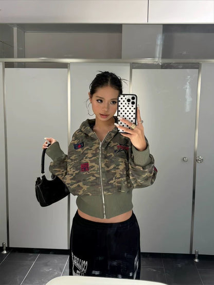 Person wearing a camouflage jacket with colorful patches in a bathroom setting.