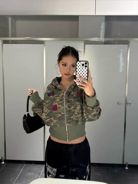 Person wearing a camouflage jacket with colorful patches in a bathroom setting.