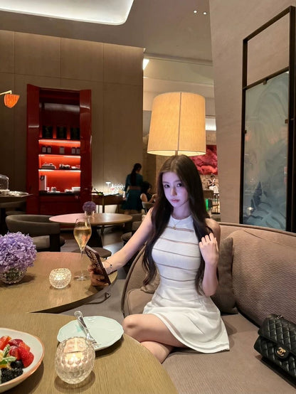 Woman in a white dress sitting on a couch in a restaurant setting with a glass of wine.