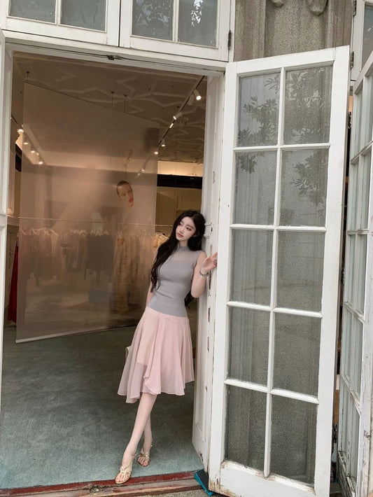 Woman standing in a doorway wearing a gray top and pink skirt.